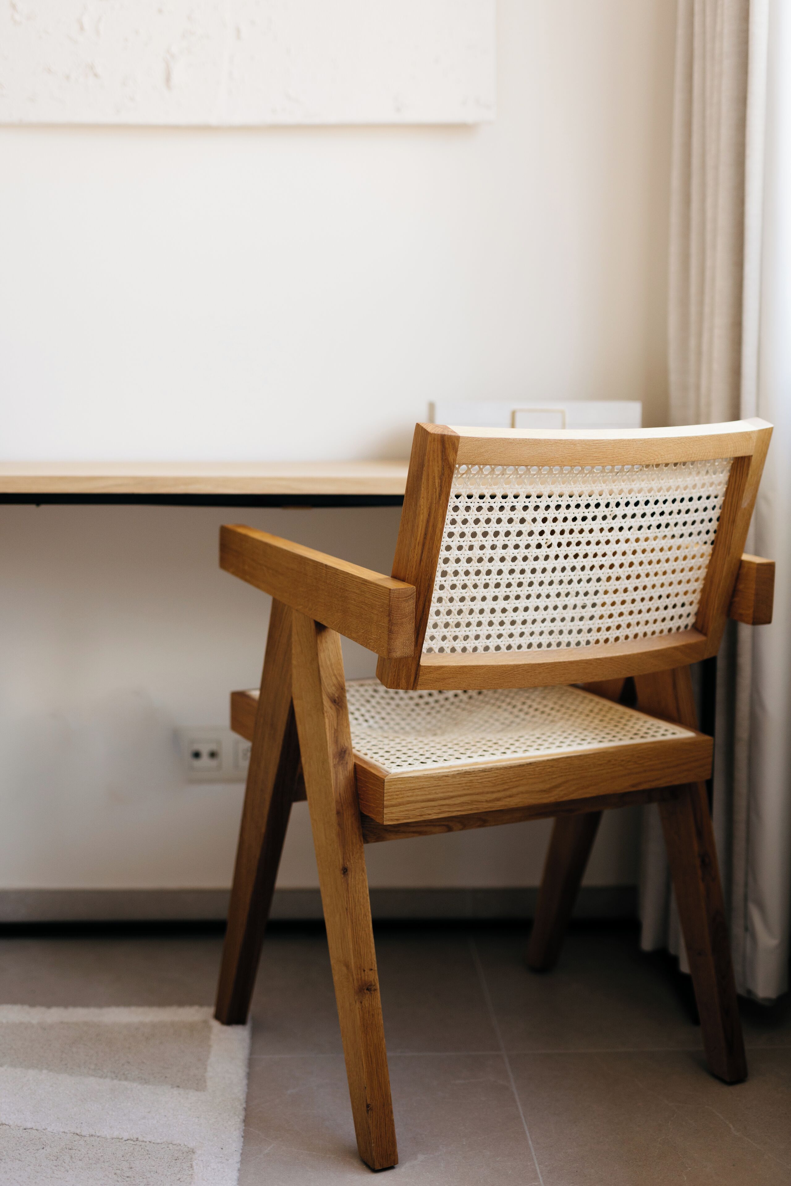 Een houten stoel met een geweven rugleuning en zitvlak, geplaatst voor een wit bureau met een kabelaansluiting.