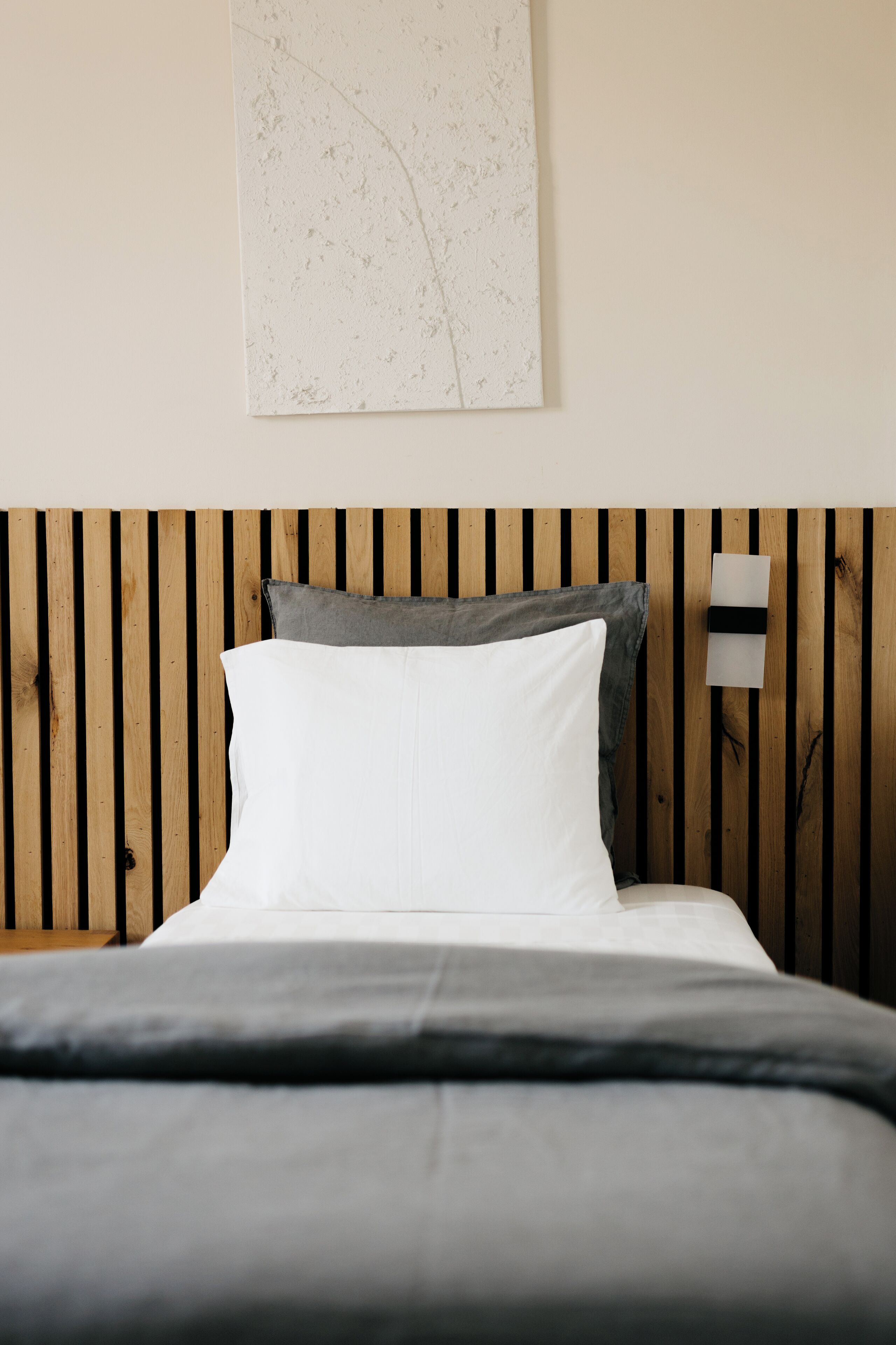 Un letto con testiera in legno, cuscini bianchi e grigi e una coperta grigia.
