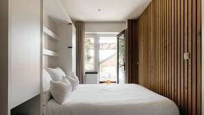 A modern bedroom with a bed, a wooden slatted wall, and a view of the outdoors. - The Edgewater Suites - Park View (Namur)