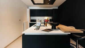 A modern kitchen with a white countertop, black cabinets, and a wooden island. - The Edgewater Suites - Park View (Namur)