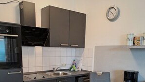A modern kitchen with dark cabinets, a built-in oven, a sink, and a coffee maker. - Apartment Strandweh with view to the deep 2 OG-House Spiekeroog Dornumersiel (Dornumersiel)