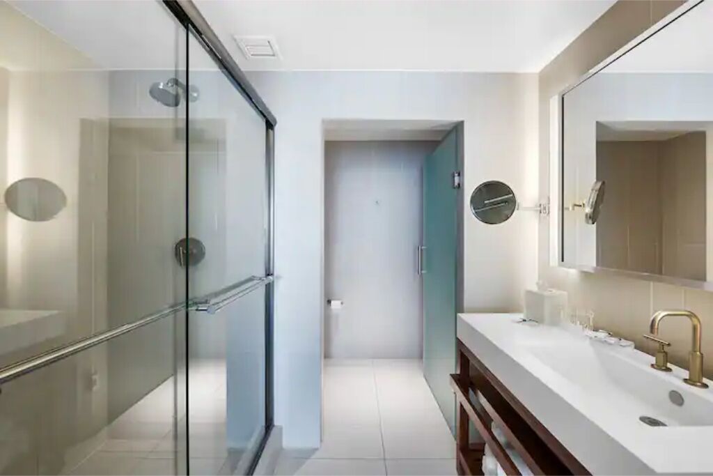A modern bathroom with a glass shower enclosure, a large mirror, and a white sink with gold fixtures.