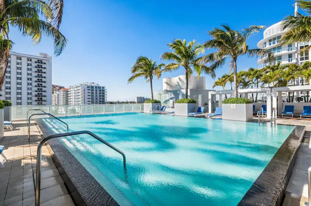 Une piscine à l’eau d’un bleu cristallin, entourée de palmiers et de chaises longues.