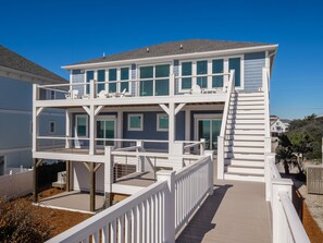 Una casa frente al mar de dos pisos con balcón, muelle de madera y barandilla blanca.