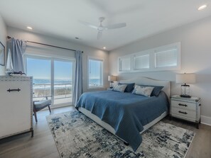 Un dormitorio con una cama grande, ventilador de techo y vista al océano a través de una puerta corredera.