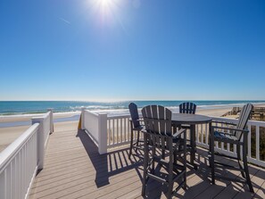 Terraza de madera con mesa y sillas con vista a la playa.