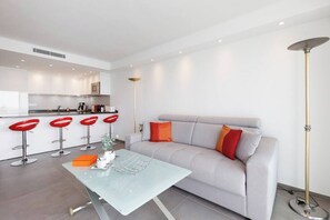 Un salon moderne avec un canapé, une table basse en verre et un coin bar doté de tabourets rouges.