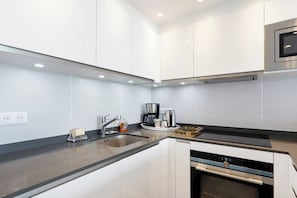 Une cuisine moderne avec des meubles blancs, une hotte en acier inoxydable, un four encastré et une machine à café.