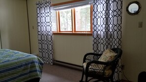 A room with a bed, a chair, a window, and a mirror on the wall.