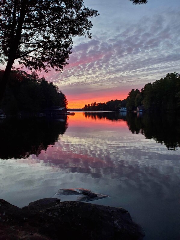 A calm lake at sunset with a tree on the left and a dock extending into the water.