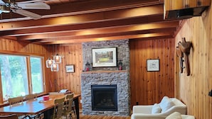 A cozy cabin interior with a stone fireplace, wooden walls, a dining area, and a seating area.