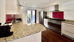 Une cuisine moderne dotée de plans de travail en granit, d’appareils électroménagers en acier inoxydable et d’un pare-feu rouge.
