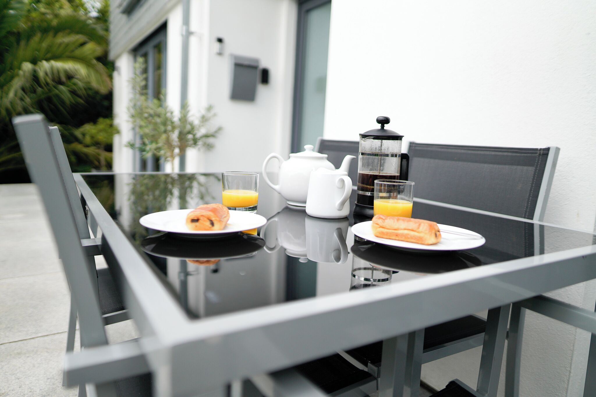 A breakfast table with a white teapot, two glasses of orange juice, and croissants on plates.