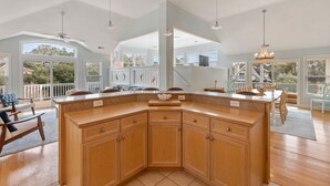 A spacious kitchen with a large island, wooden cabinets, and a view of the outdoor deck. - Koselig Kove: Private Pool | Hot Tub | Rec Room (Corolla)