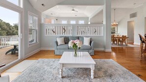 A spacious living room with a light blue sofa, a white coffee table, and a large window. - Koselig Kove: Private Pool | Hot Tub | Rec Room (Corolla)
