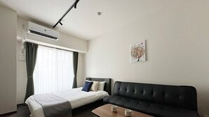A hotel room with a bed, a sofa, a coffee table, and an air conditioning unit. - Nagomi by b hotel | Comfortable Studio Stay N41 (Hiroshima City)