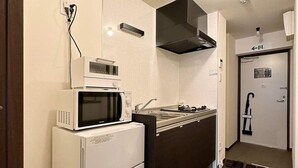 A compact kitchen with a microwave, oven, and sink. There is a black range hood above the stove. A door with an emergency exit sign is visible in the background. - Nagomi by b hotel | Comfortable Studio Stay N41 (Hiroshima City)