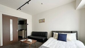 Una habitación de hotel con cama, sofá, una mesita y kitchenette.
