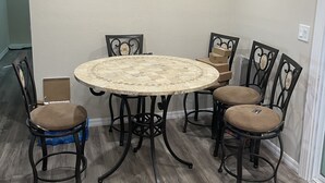 Een eetgedeelte met een ronde tafel en zes stoelen, een houten vloer en een lichtgekleurde wand.
