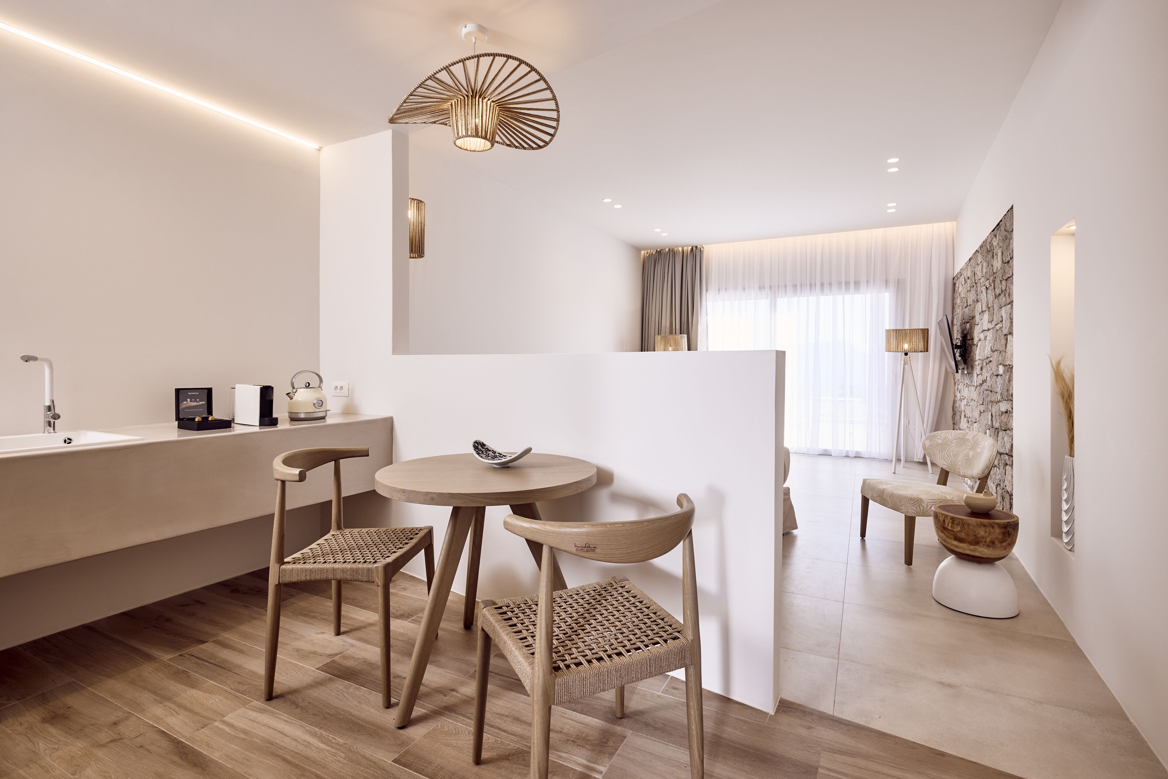 A modern, minimalist room with a wooden floor, a round table with two chairs, a white partition, and a stone accent wall.