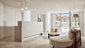 A modern interior with a reception desk, a cushioned seating area, and large windows offering a view of the outdoors. - Civitas Milos (Milos)