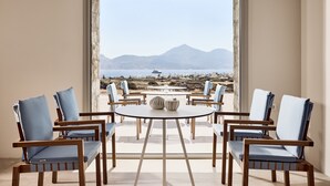 A balcony with a round table and six chairs, offering a view of a mountainous landscape and a body of water. - Civitas Milos (Milos)