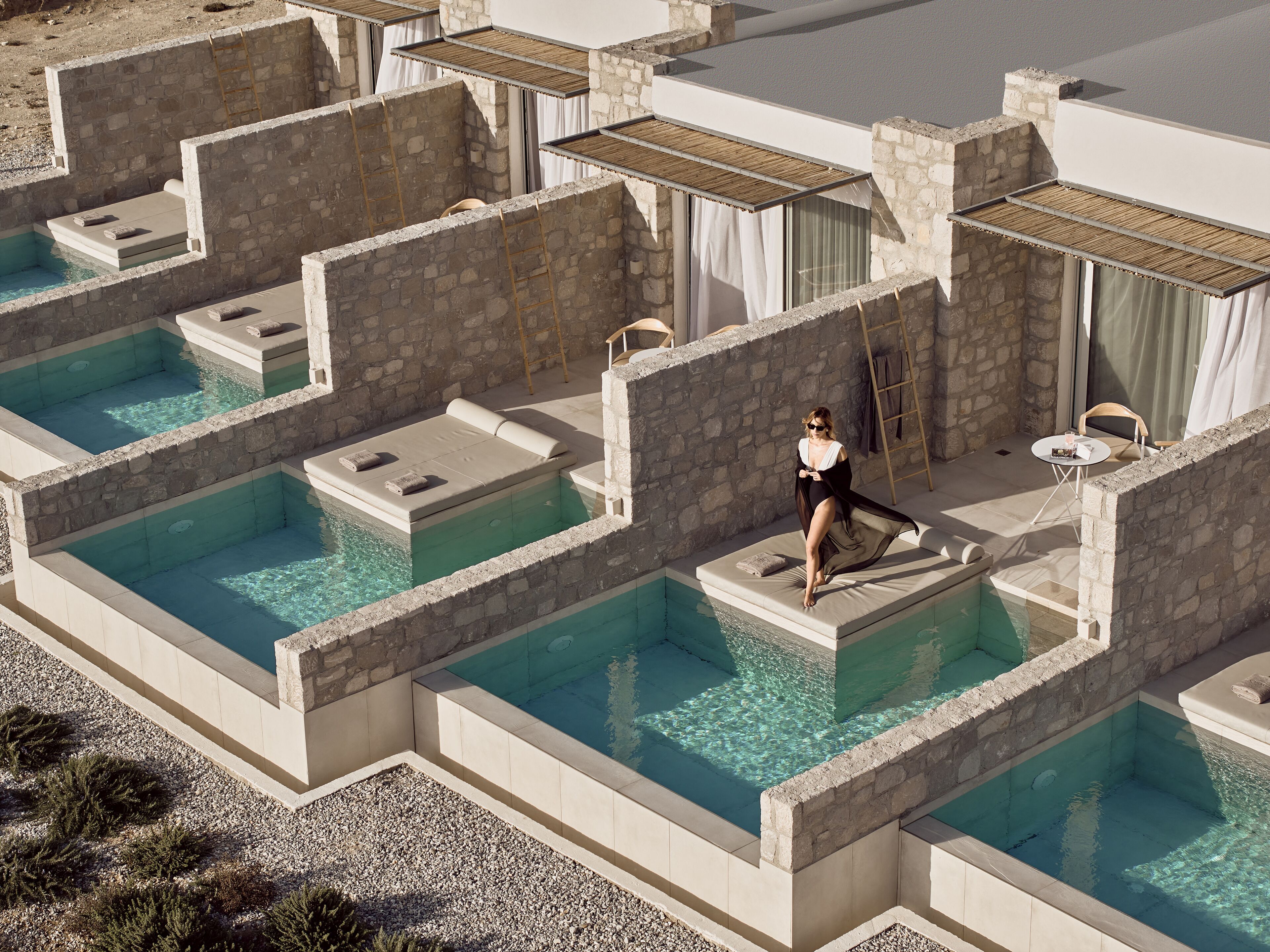 A pool area with multiple small pools, stone walls, and a person sitting on a poolside.
