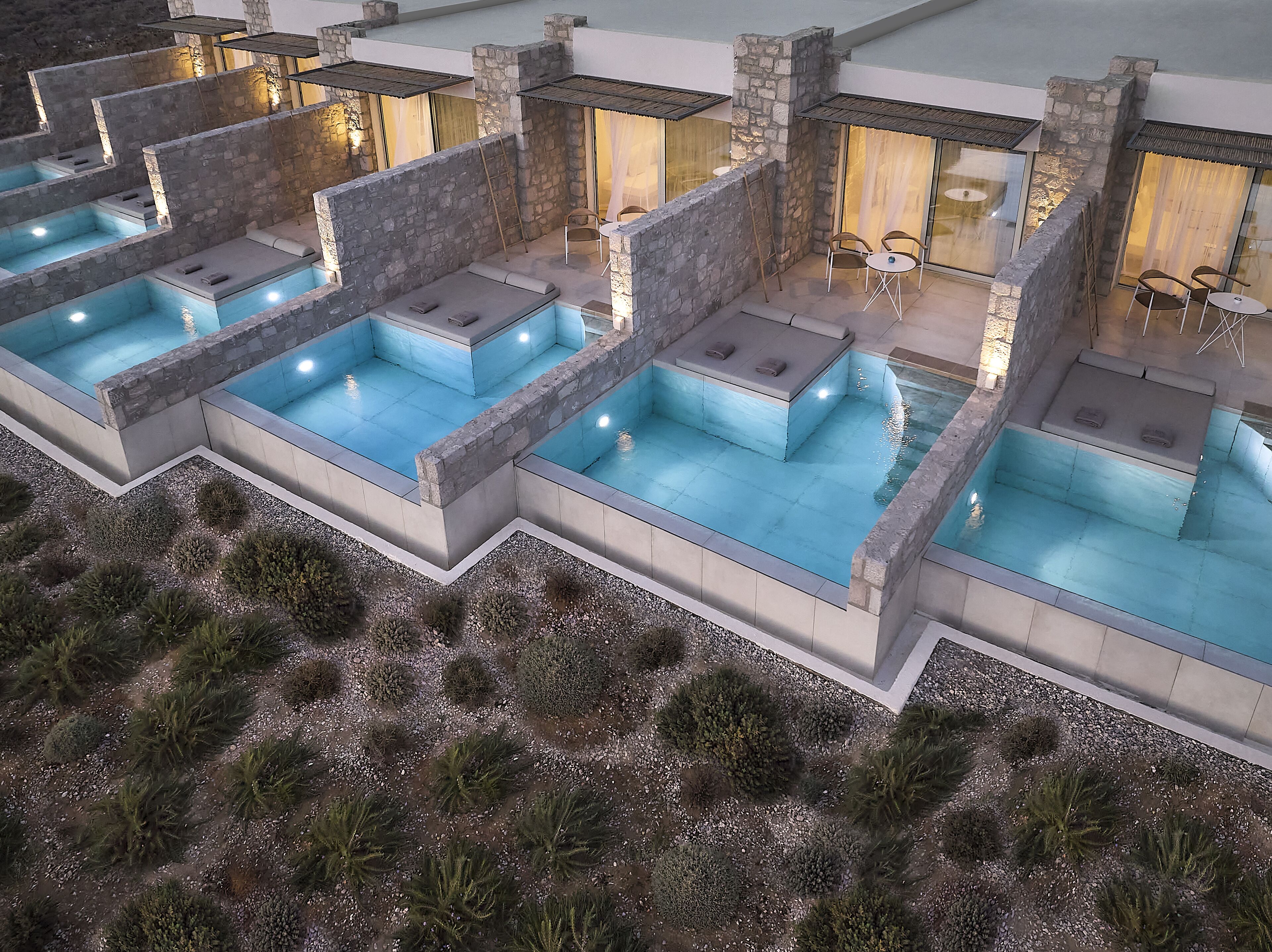 Un área de piscina moderna al aire libre con varias piscinas, muros de piedra y zonas de estar.