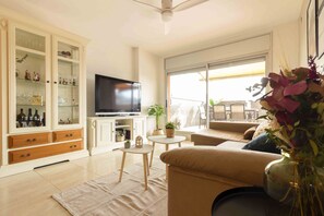 Una sala de estar con televisor, sofá, una mesita y un mueble con puertas de vidrio.