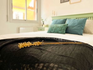 Una cama con cabecera verde, almohada negra y ventana con vista a un edificio.