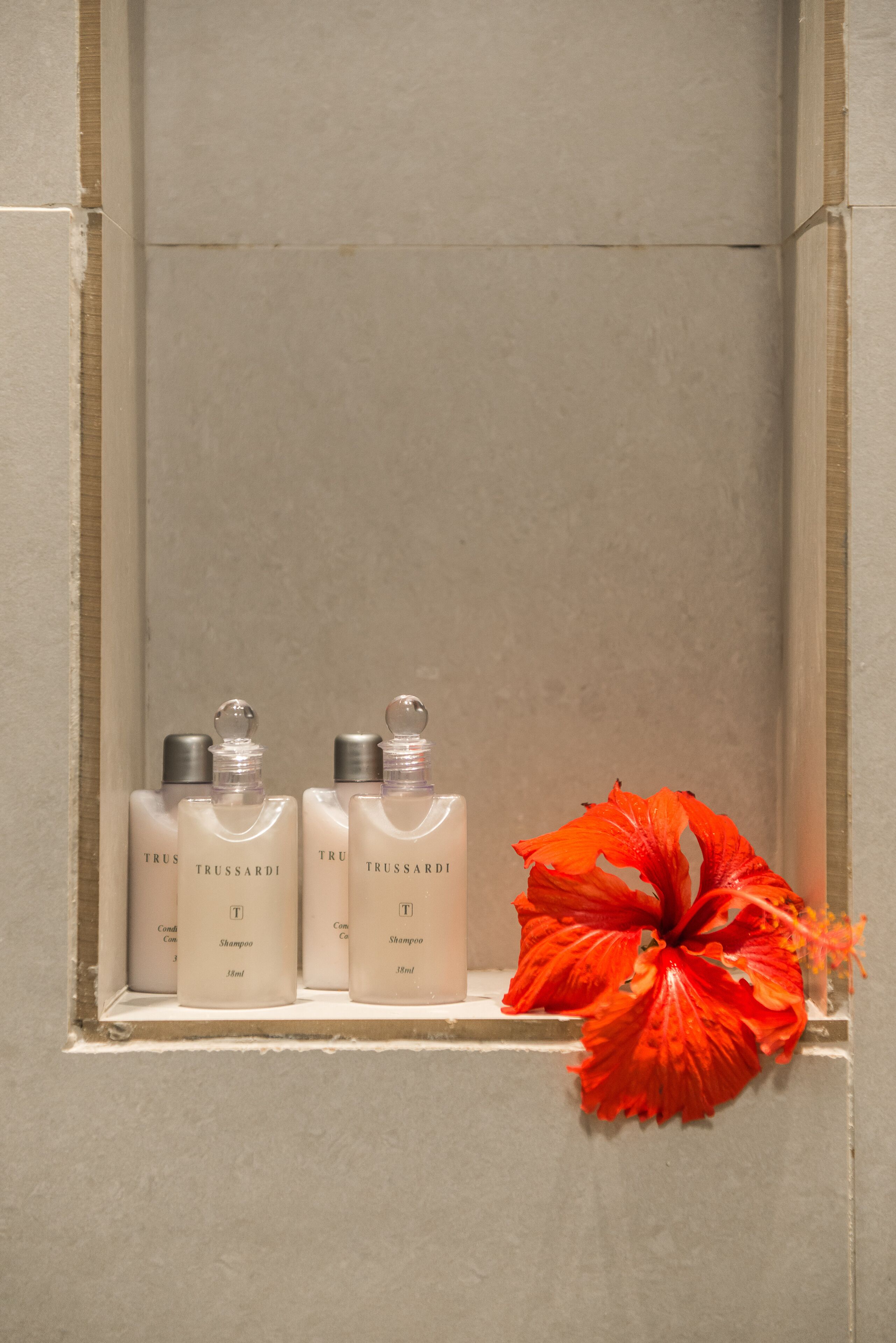 A shelf with three bottles of Trussardi shampoo and a red flower.