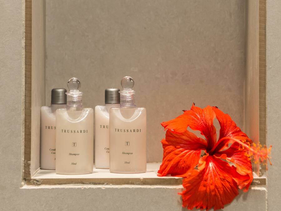 A shelf with three bottles of Trussardi shampoo and a red flower.