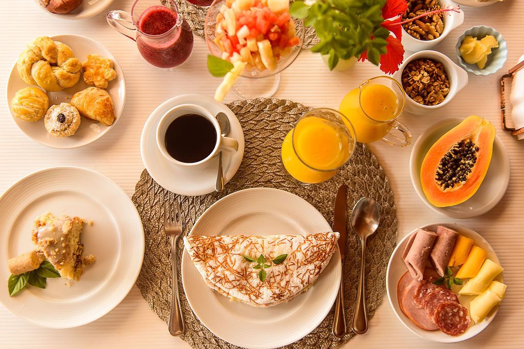 A breakfast table with various foods and drinks, including pastries, fruit, and a rolled omelette.
