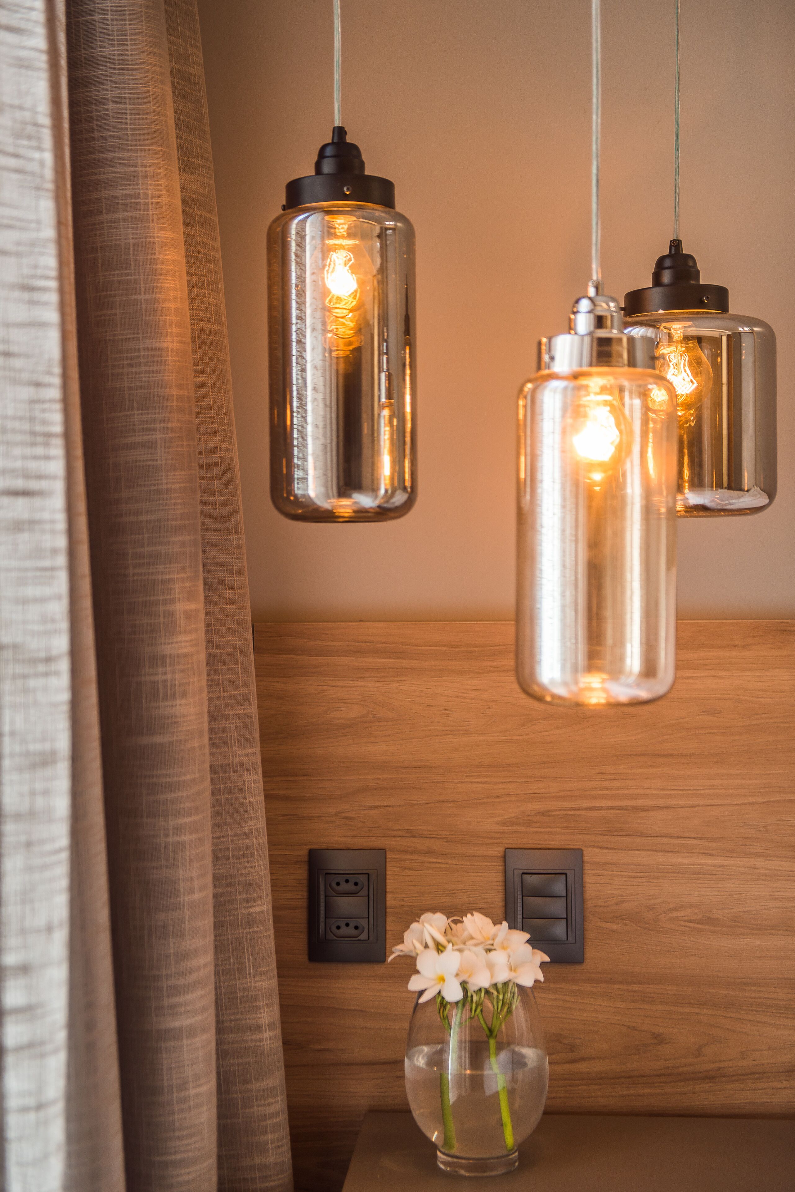 A modern interior with pendant lights, a wooden panel wall, a power outlet, and a vase with flowers.