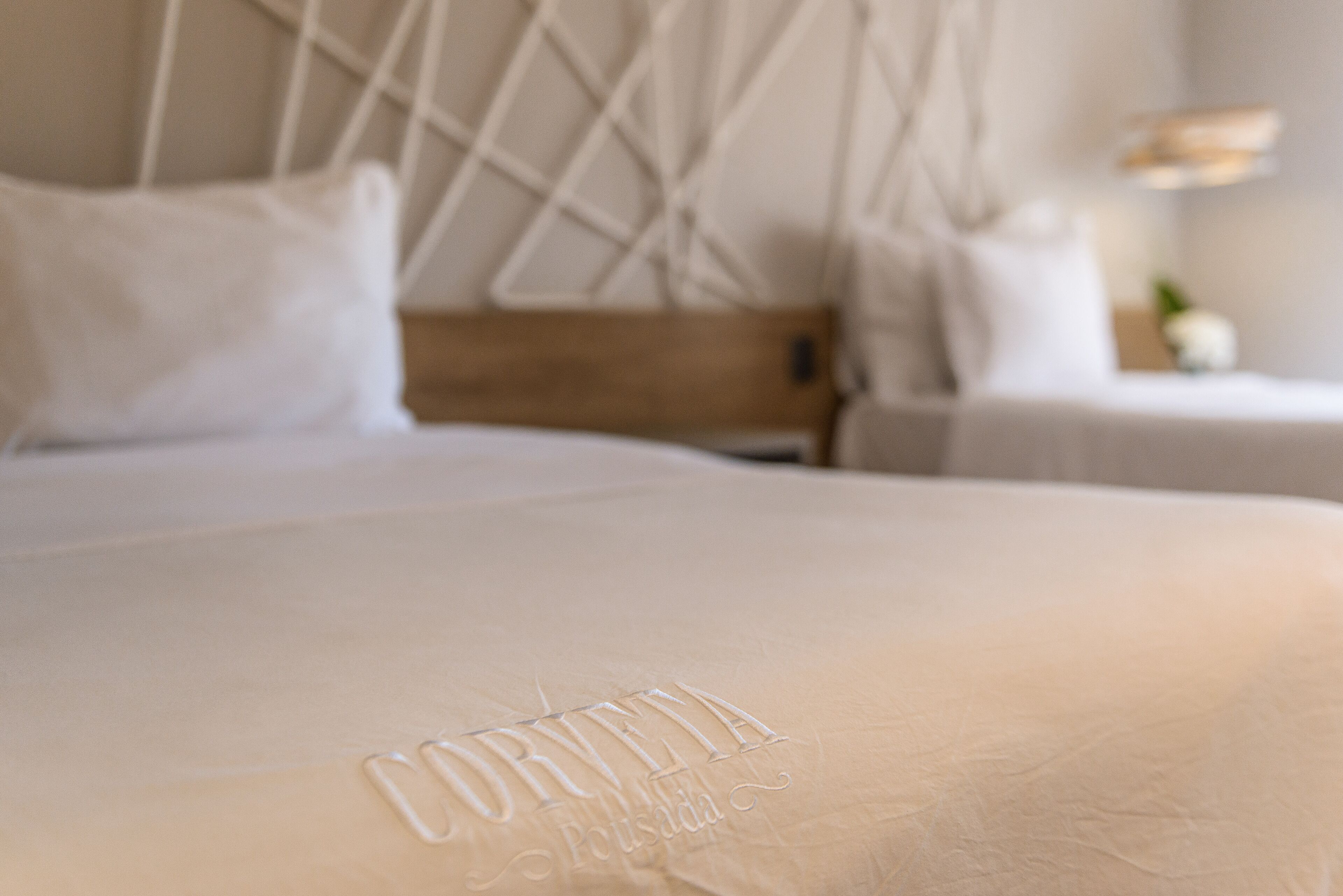 Ein Bett mit weißem Kopfteil und einem Kissen mit dem Schriftzug 'CORVETA Pousada'.