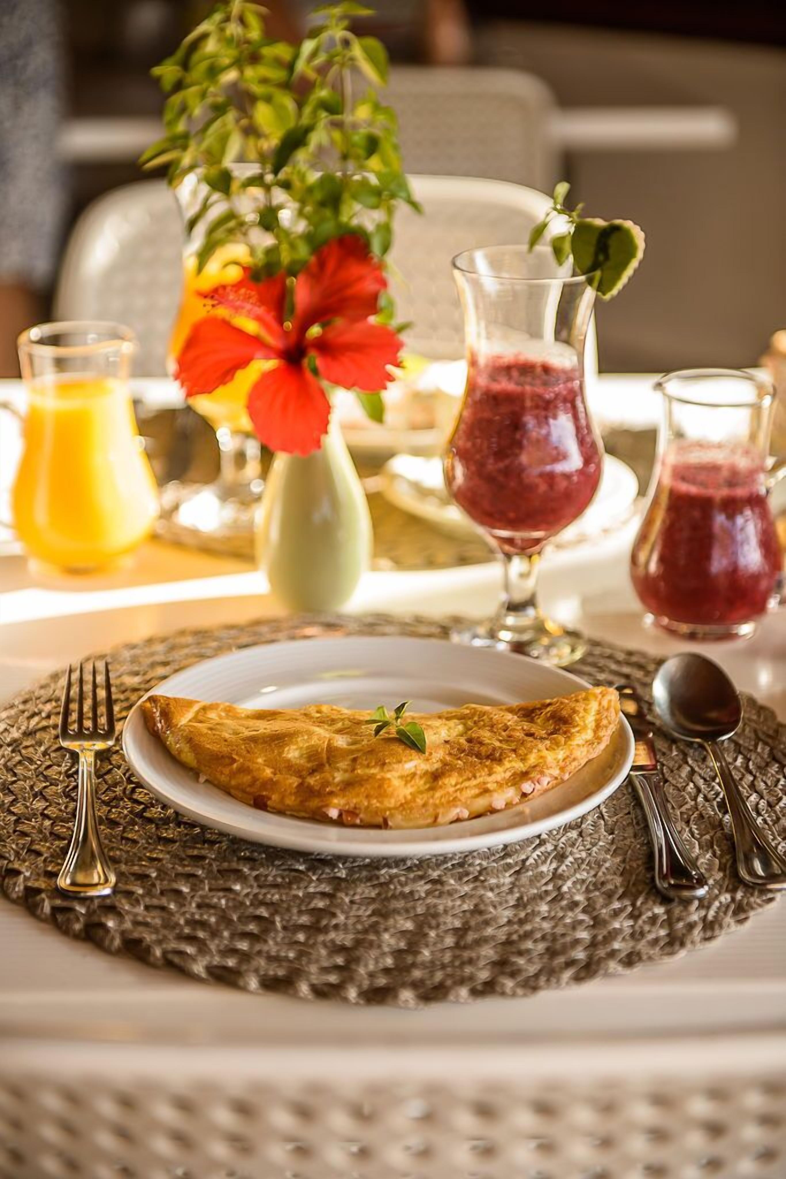 A breakfast setting with a plate of food, a glass of orange juice, and two glasses of red juice.