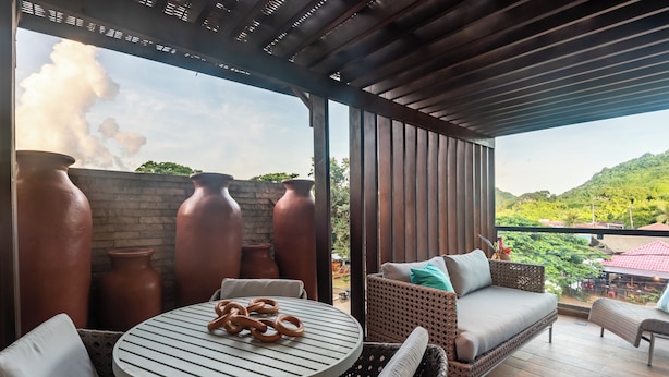 A covered patio with wicker furniture, a round table with pretzels, and terracotta pots.