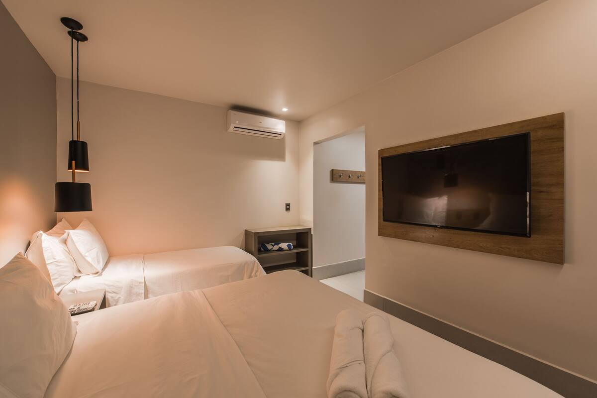 A hotel room with two beds, a TV mounted on the wall, a bedside table, and a wardrobe.