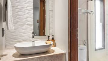 A modern bathroom with a large oval sink, a mirror, a shower, and a toilet.