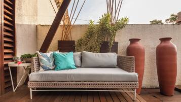 Un canapé blanc agrémenté de coussins à motifs, une petite table avec des plantes et deux grands pots en terre cuite sur une terrasse en bois.