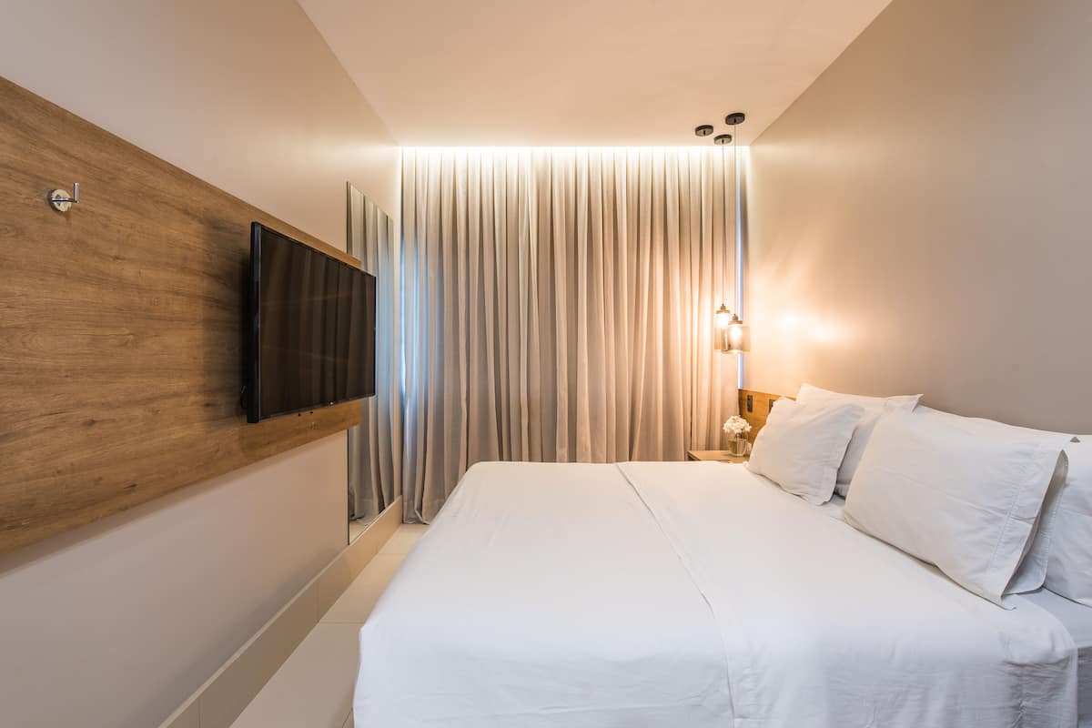 A modern hotel room with a large bed, a mounted TV, and a curtain divider.