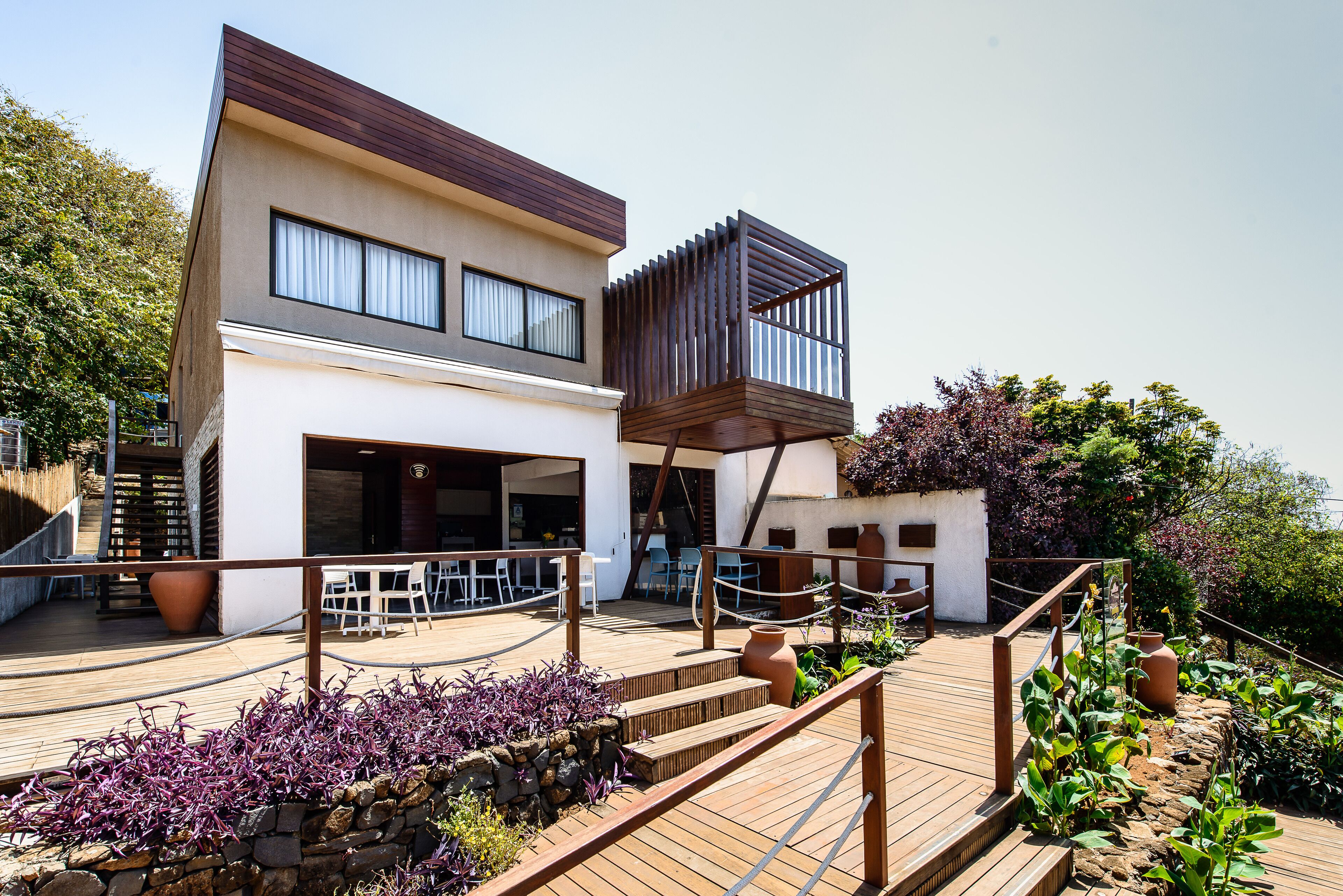 Un edificio moderno de dos pisos con balcón, zona de estar exterior y terraza de madera.