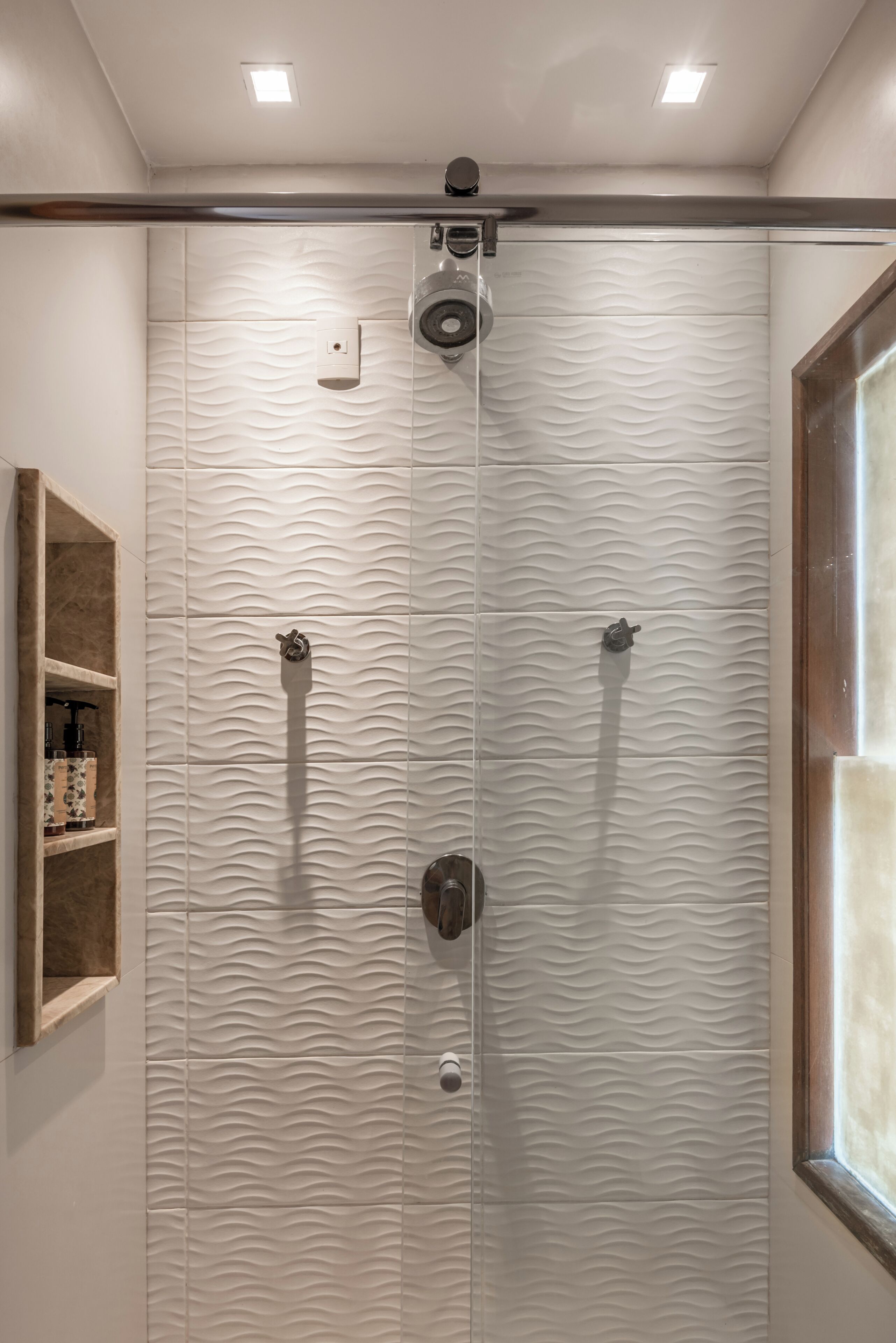 A shower with a textured wall and a shelf with toiletries.
