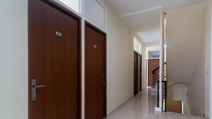 A hallway with two wooden doors, a tiled floor, and a staircase leading to an upper level. - OYO 3216 Ellegan Residence (South Tangerang)