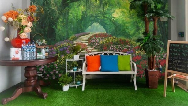 A room with a mural of a forest, a white bench with colorful cushions, a small table with a vase of flowers, and a chalkboard menu. - OYO 3216 Ellegan Residence (South Tangerang)