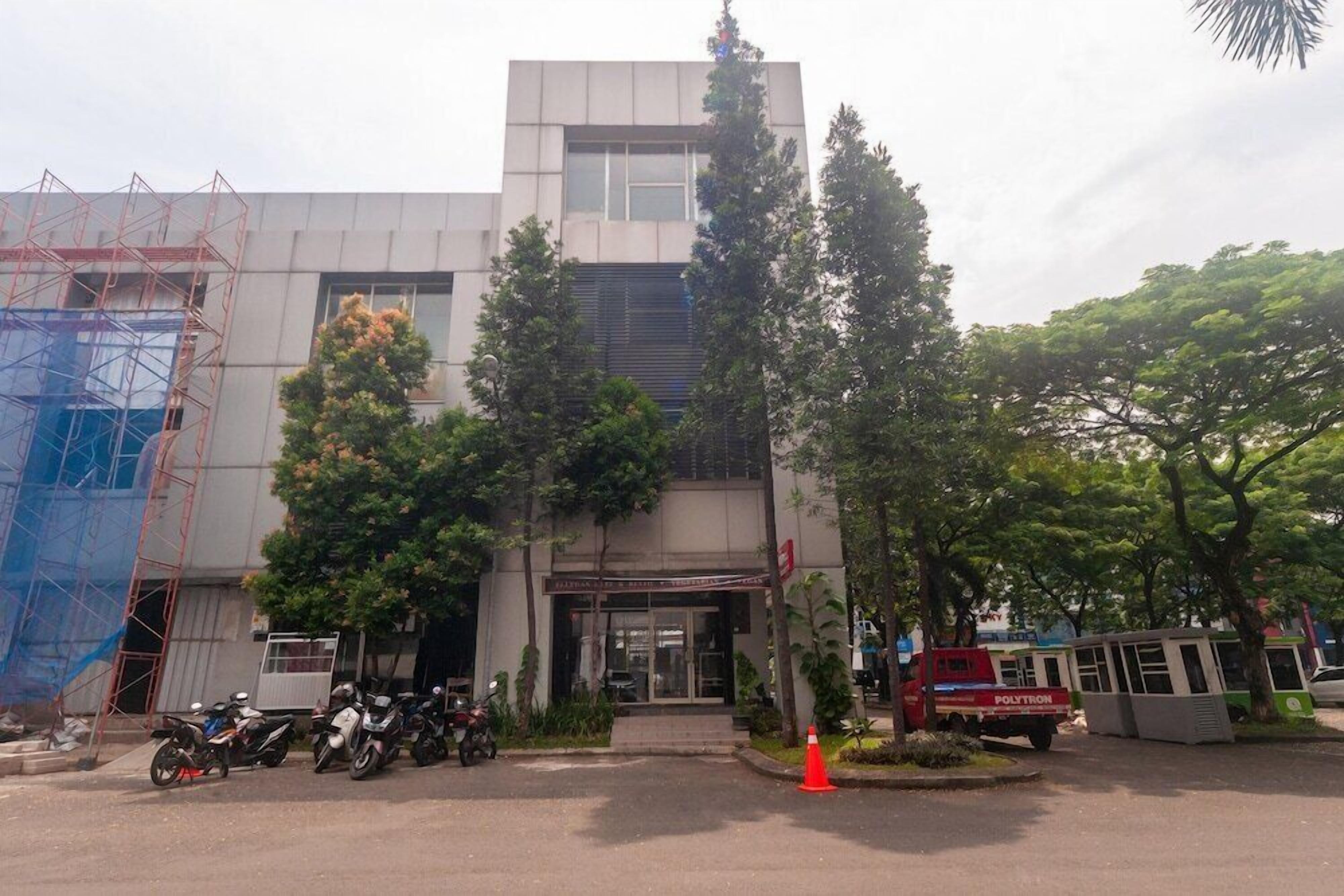 A building with a modern architectural style, featuring a central entrance with glass doors, surrounded by trees and parked vehicles.