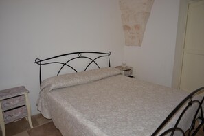 A single bed with a metal frame, a bedside table with a lamp, and a small dresser with drawers.