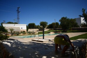 Una piscina con un muro de piedra, una estructura metálica y un cielo azul despejado.