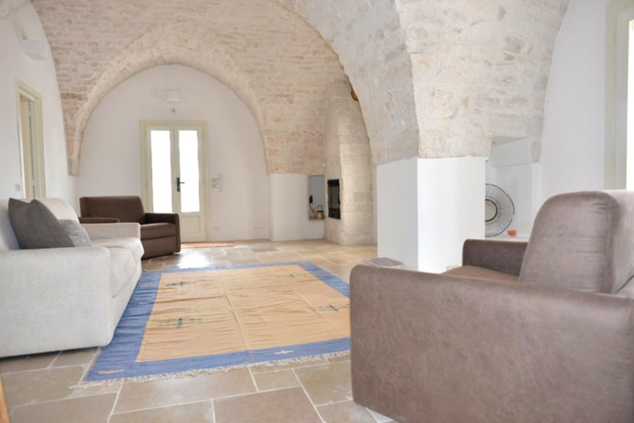 A spacious living room with a high arched ceiling, a large window, and a stone wall.