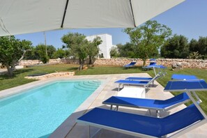 A swimming pool with blue lounge chairs and a white building in the background.